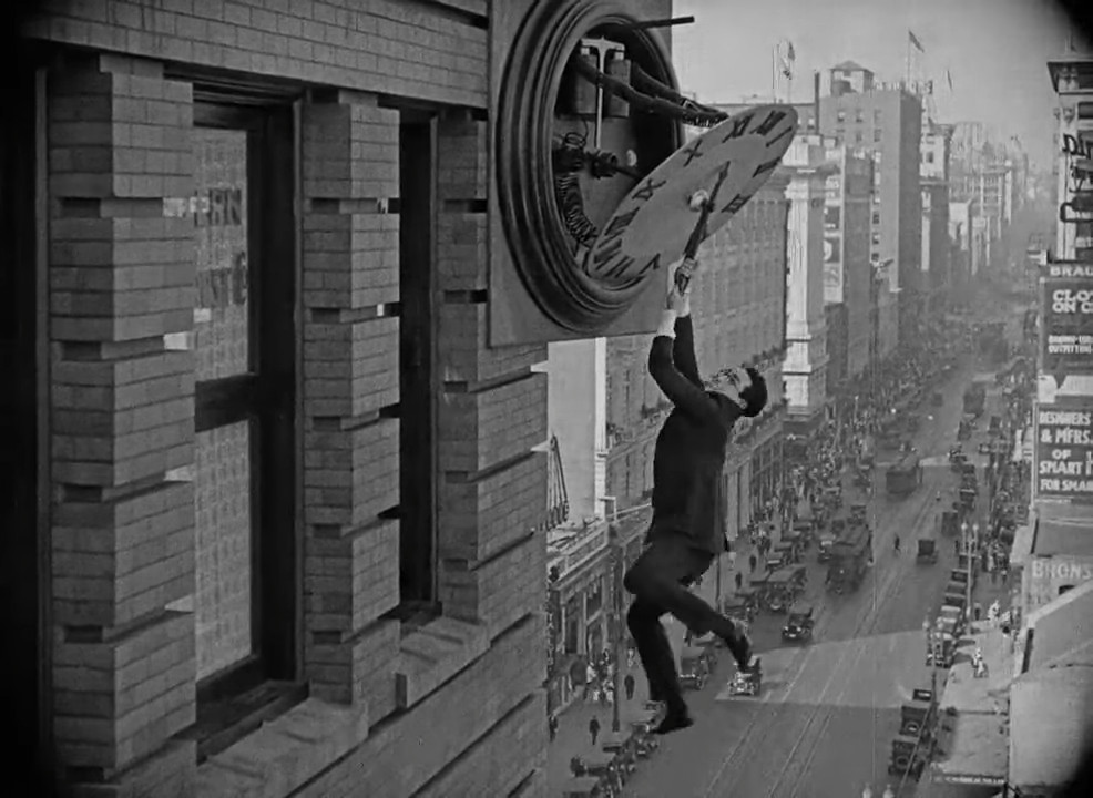 Screenshot of movie “Safety Last!” with Harold Lloyd hanging from a clock on a building’s façade.
